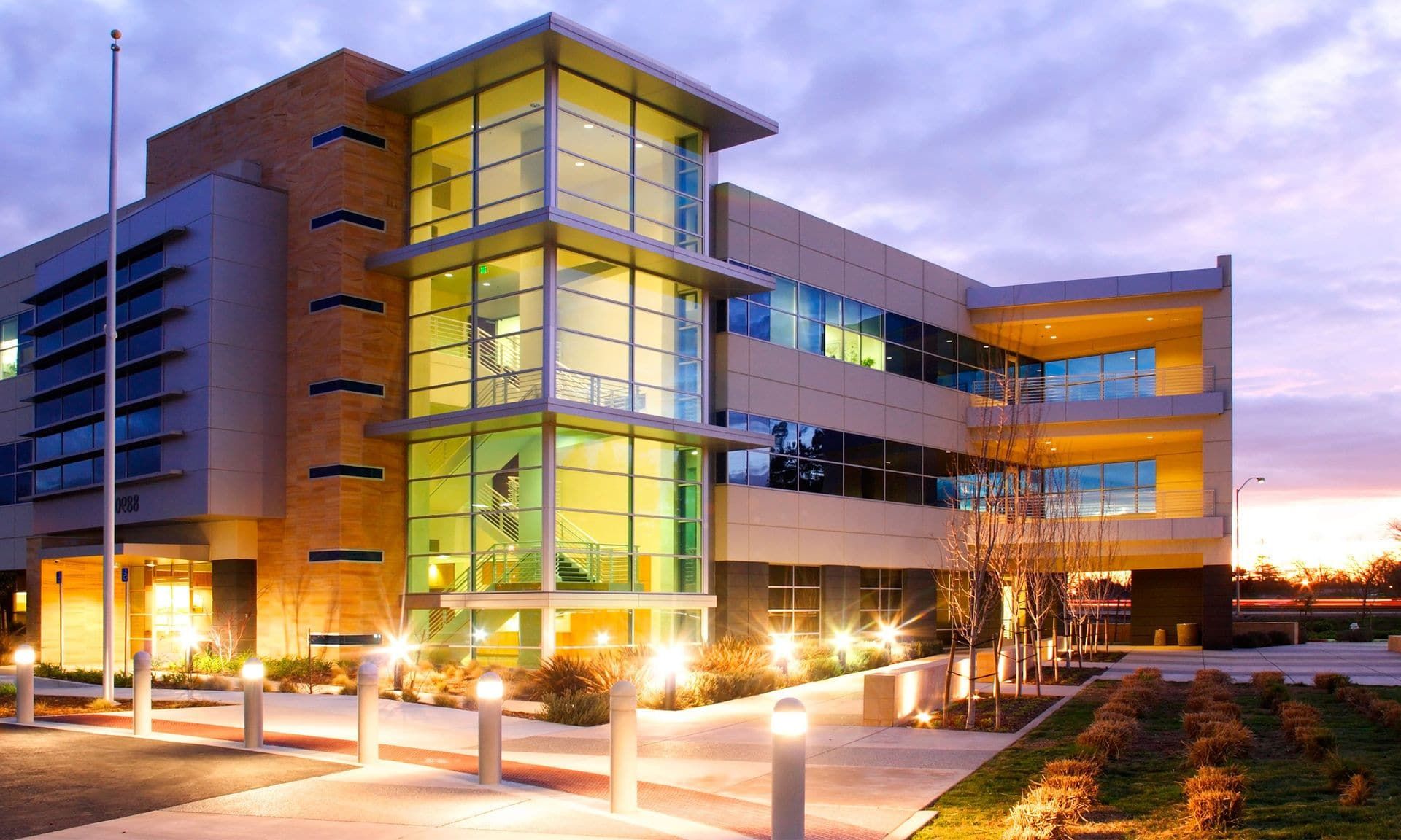 A lit commercial office building at dusk with illuminated parking-lot lighting